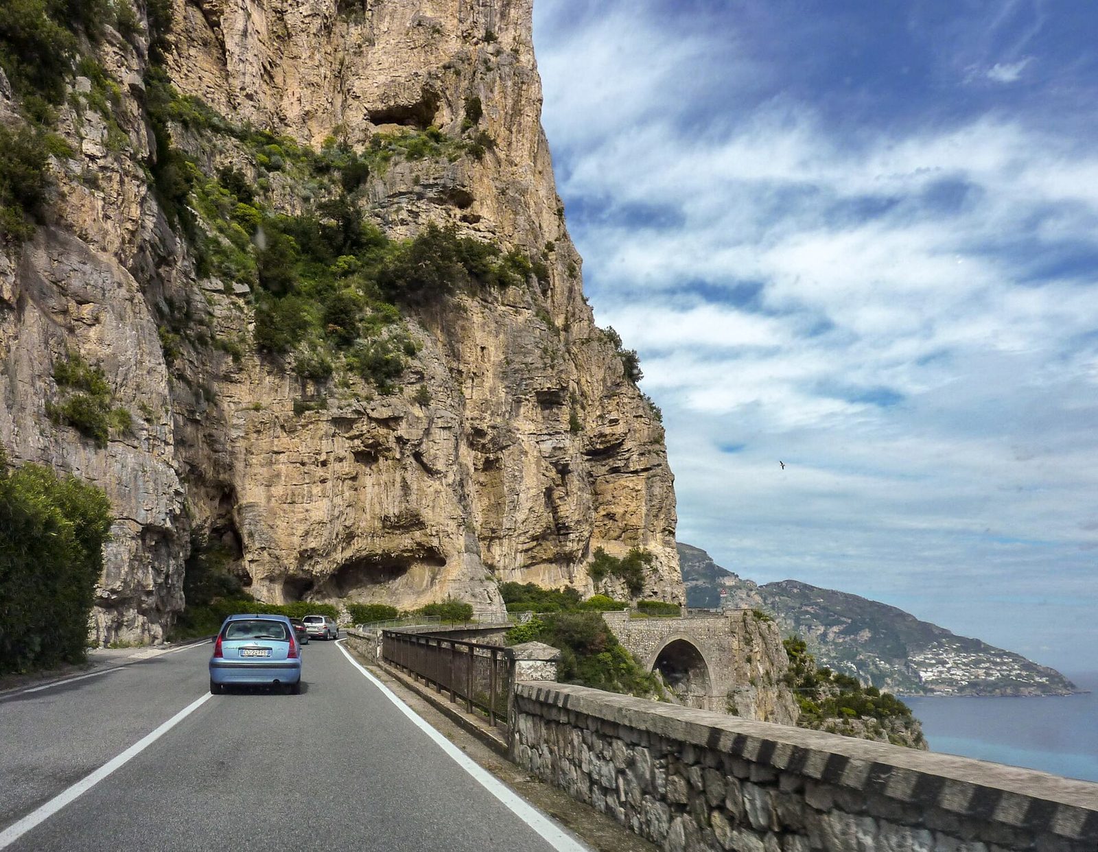 The SS163 Amalfi Coast road cut into the cliff above the sea, with a car approaching a tunnel