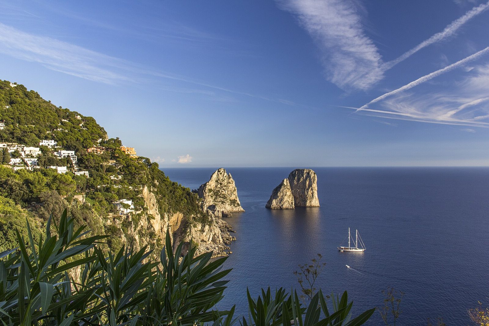 The Faraglioni rocks off Capri with a sailboat on the blue sea, a highlight of any boat tour around the island