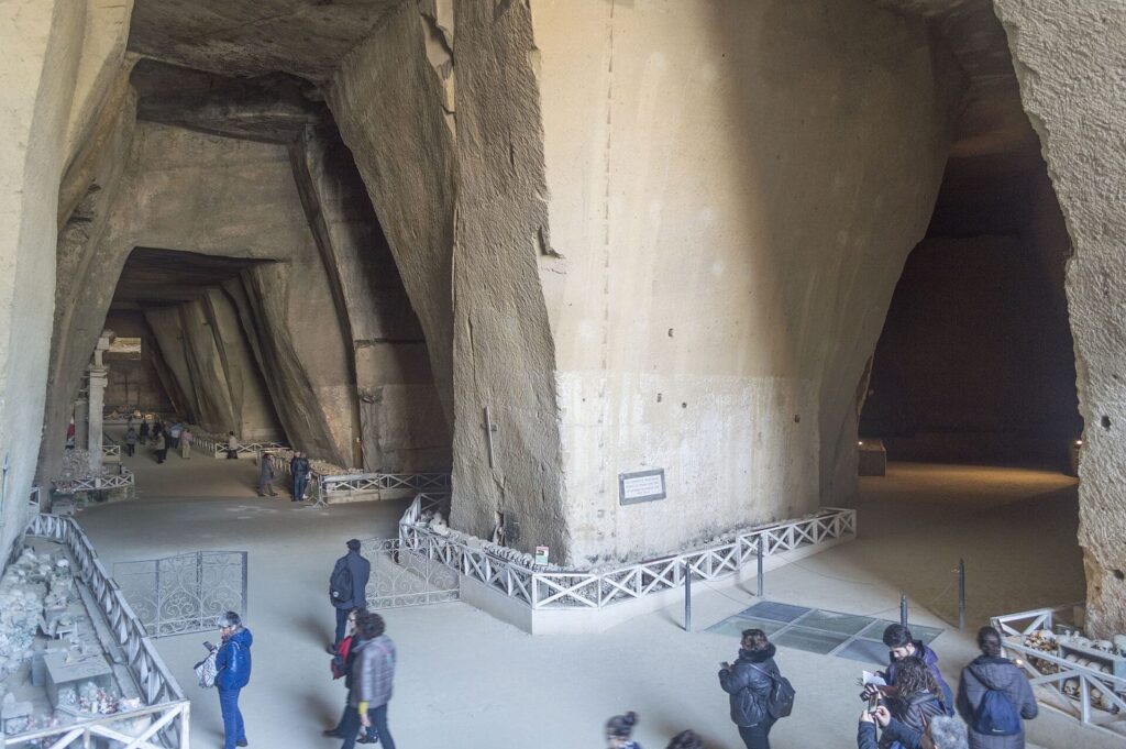Visitors walking through the vast tuff quarry caverns of the Cimitero delle Fontanelle ossuary in Naples