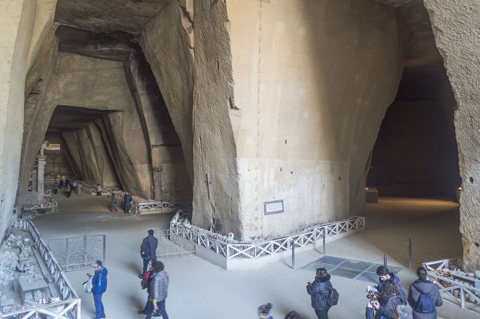 Visitors walking through the vast tuff quarry caverns of the Cimitero delle Fontanelle ossuary in Naples