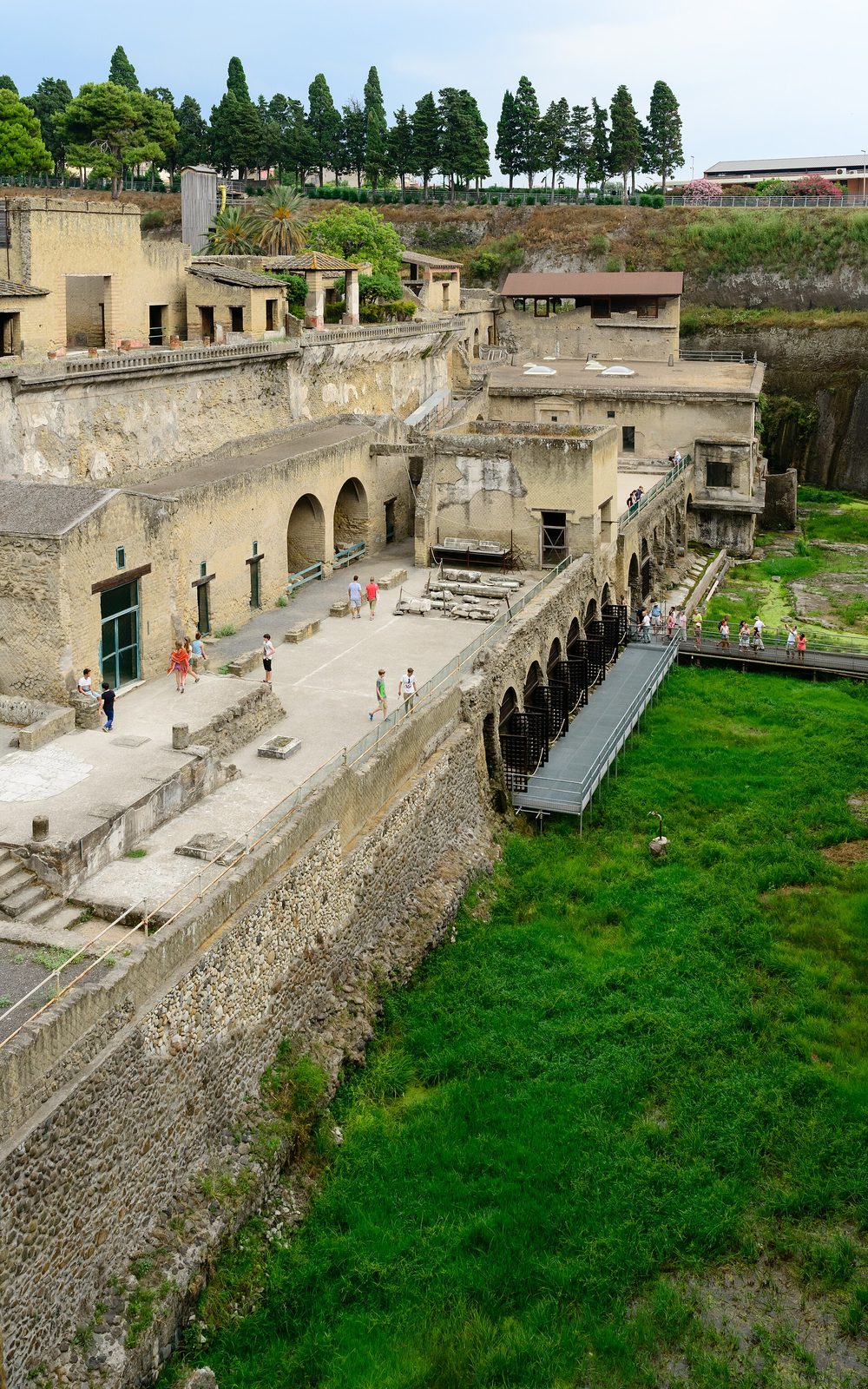 The tall walls of the ancient shoreline at Herculaneum, with the excavated houses above and the green former beach below
