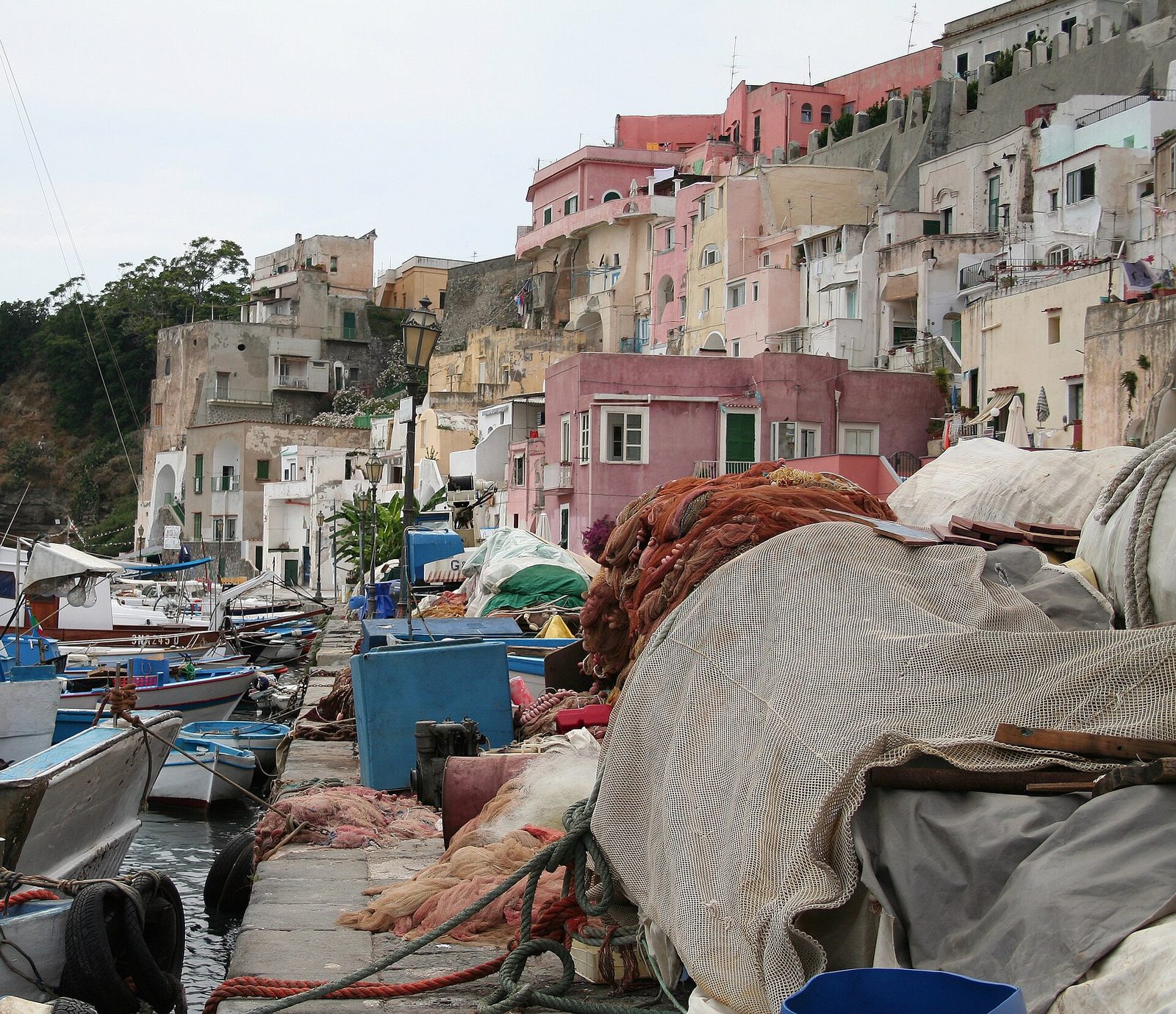 Procida, Italy: fishing nets and boats on the quay of Marina Corricella, with pastel houses climbing the cliff