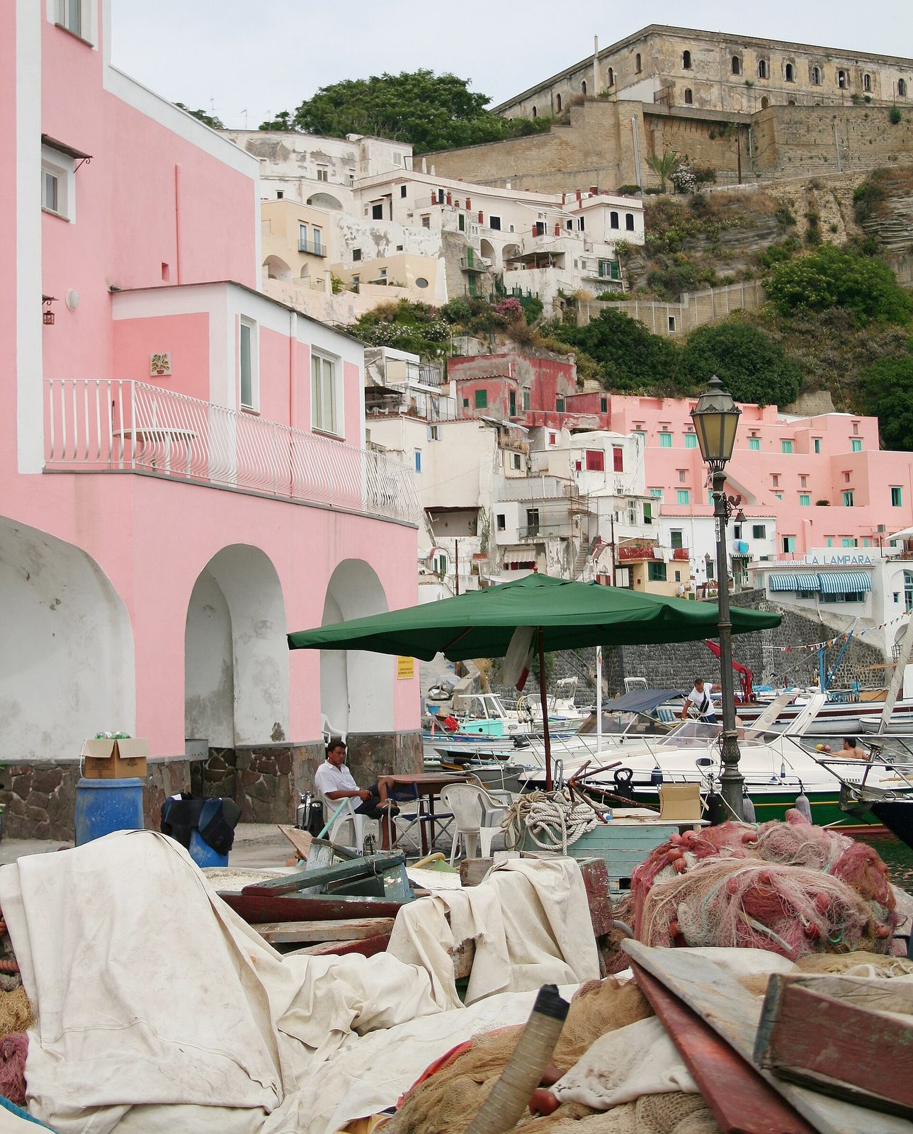Pink and pastel houses of Marina Corricella on Procida, with Terra Murata's walls on the hill above
