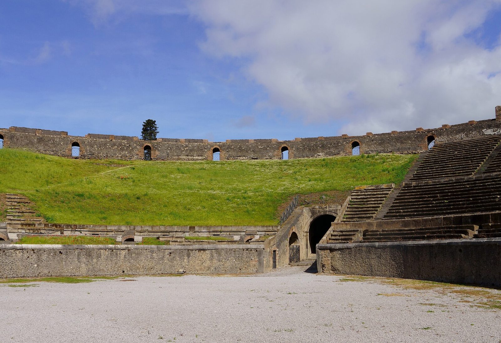The arena inside the Roman amphitheater at Pompeii, with stone seating tiers around a grassy field