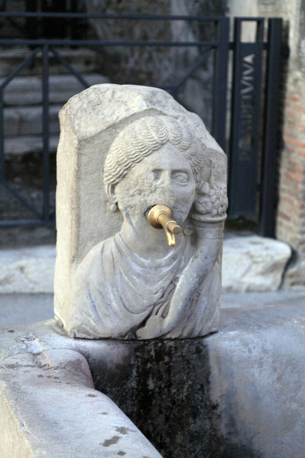 A carved stone street fountain with a woman's face on Via dell'Abbondanza in Pompeii