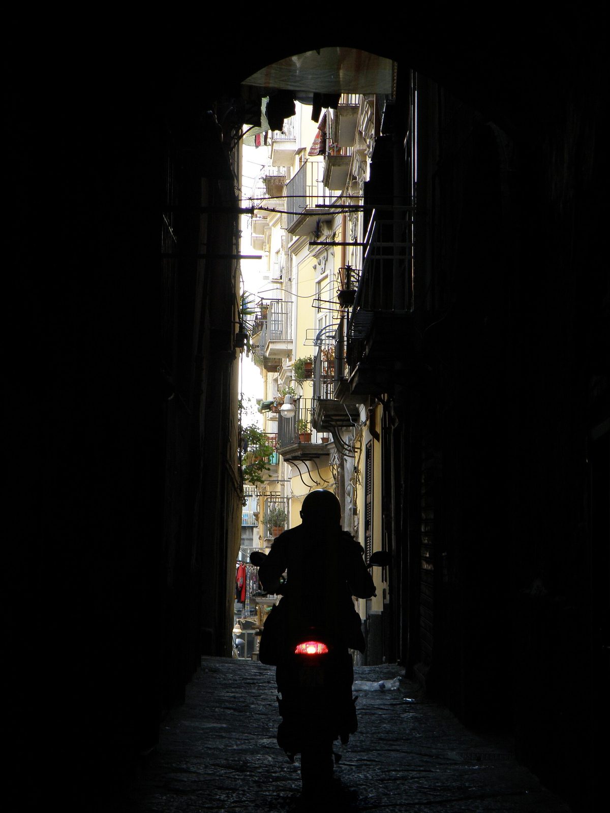 A scooter rider passing through a narrow, dark alley in the historic center of Naples