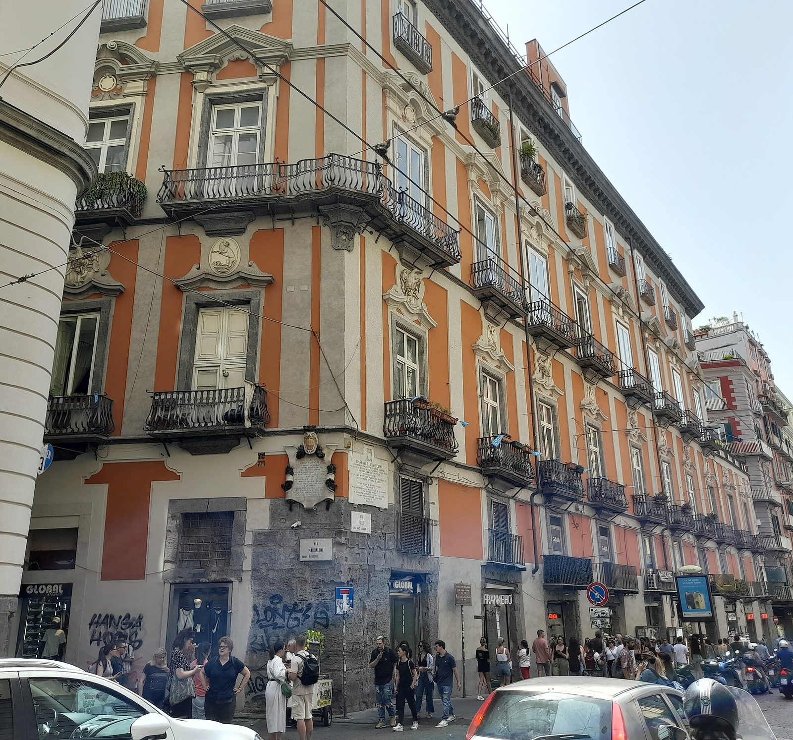 Crowds and traffic on Via Toledo in front of the orange Palazzo Carafa di Maddaloni in Naples