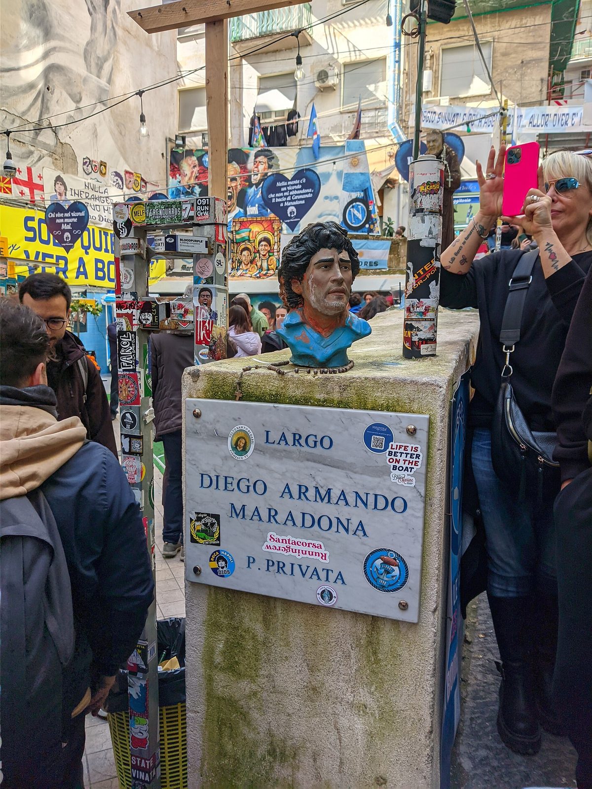 The Largo Diego Armando Maradona street sign with a bust of Maradona and fans around it