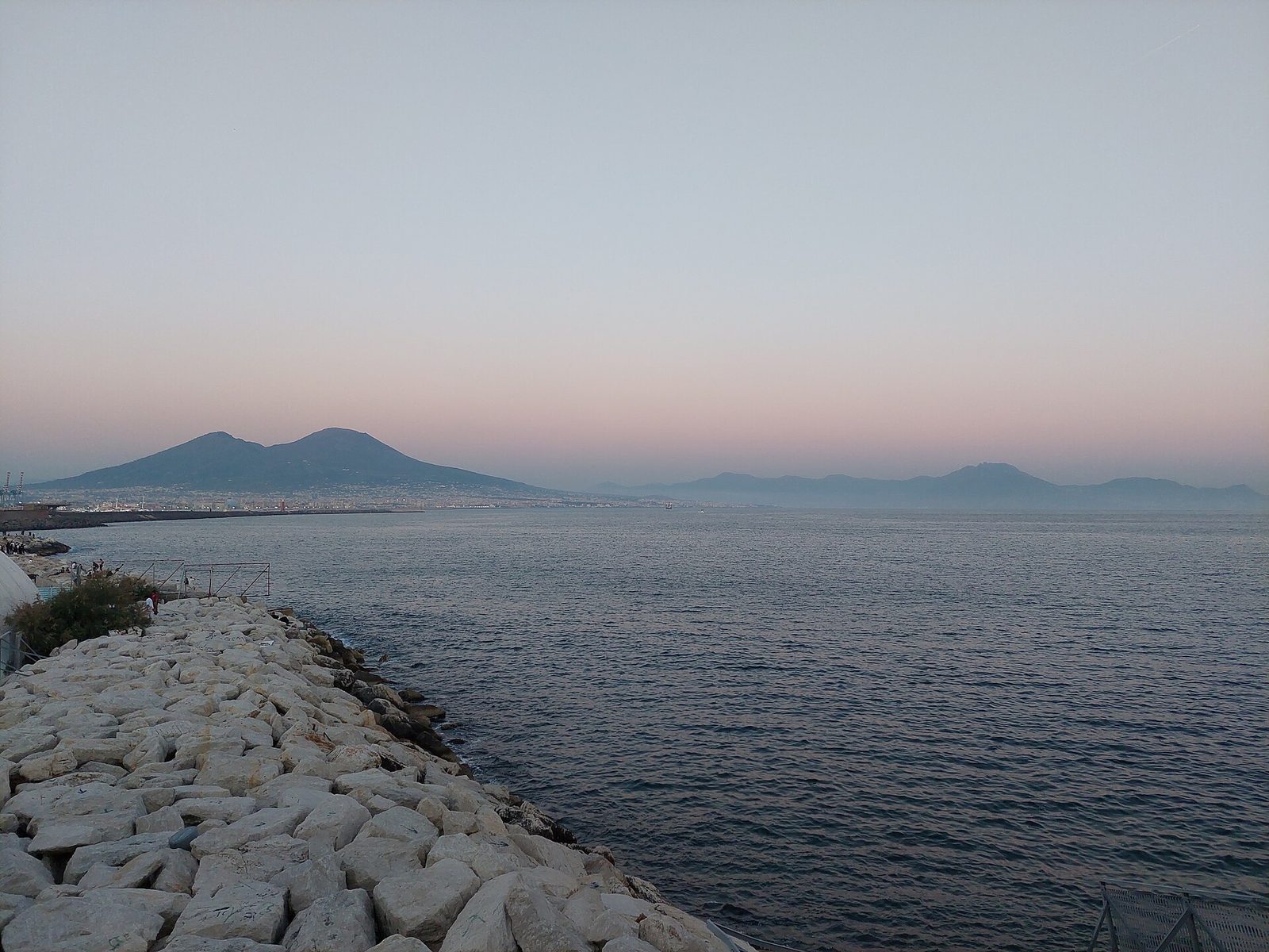 The Naples seafront at dusk with the breakwater and Vesuvius on the horizon